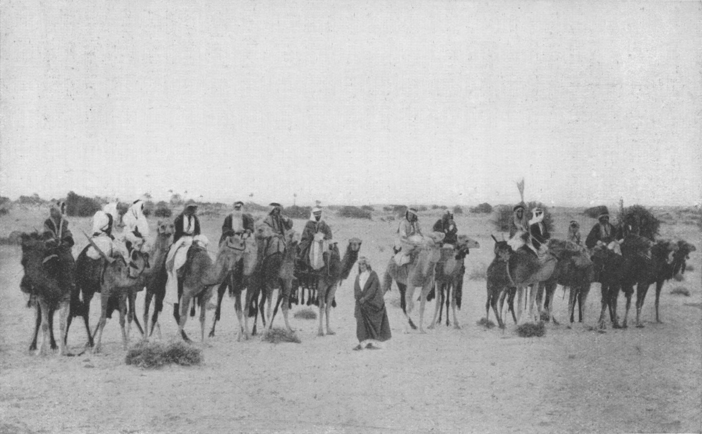 Photo wide shot of Lawrence standing in a line of
                Arabs on camels