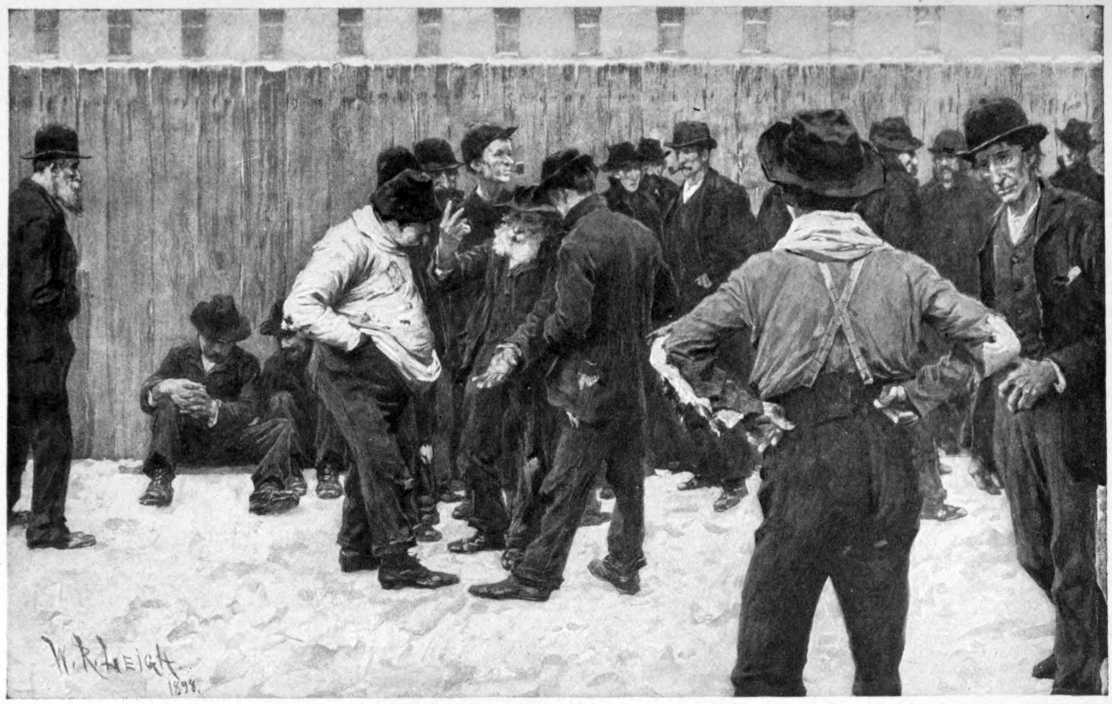 Men gathered outside. A fence
is visible behind them with a wide building visible behind the fence.