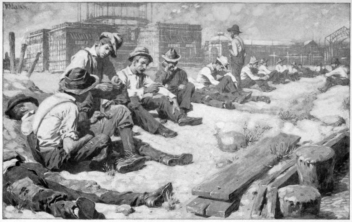 Men sitting on ground with factories in the background.