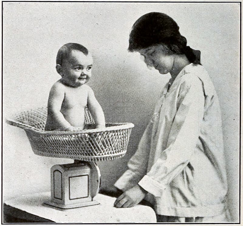 A baby in a basket on a scale
that is being read by a woman